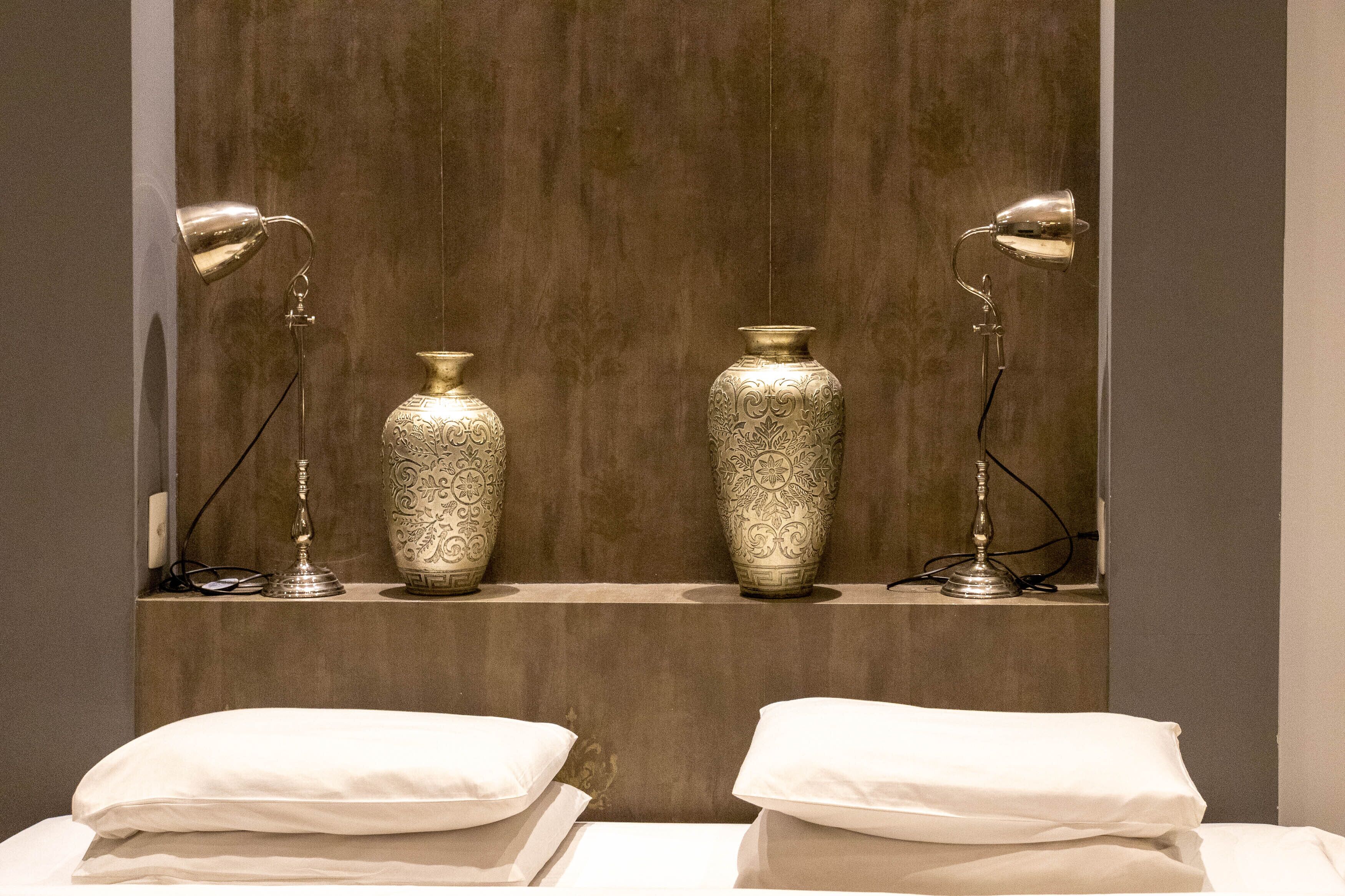 Une chambre d’hôtel avec deux grands vases posés sur une étagère, deux lampes de chevet et deux oreillers blancs sur le lit.