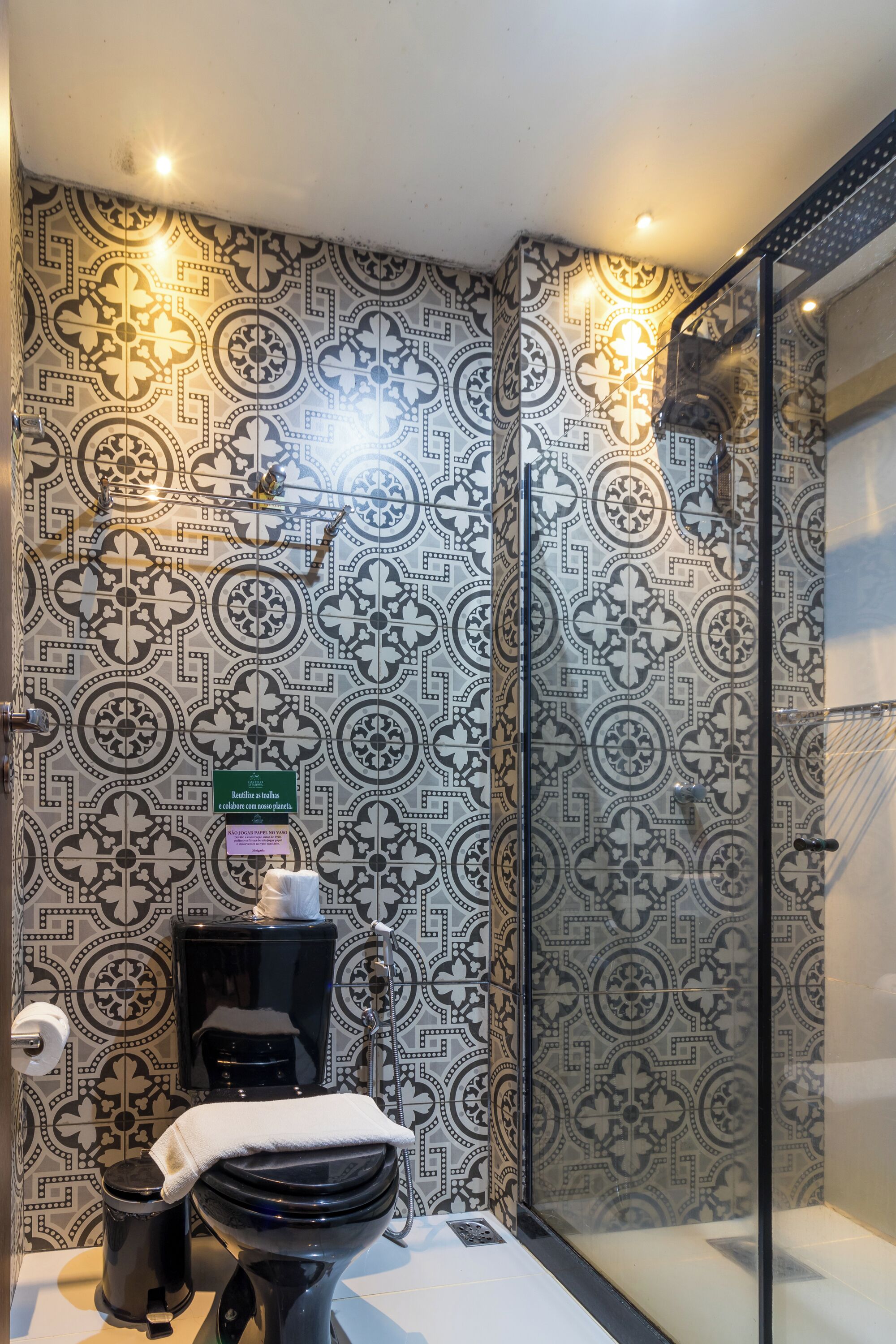 A bathroom with patterned tiles, a toilet, a trash bin, and a glass shower enclosure.
