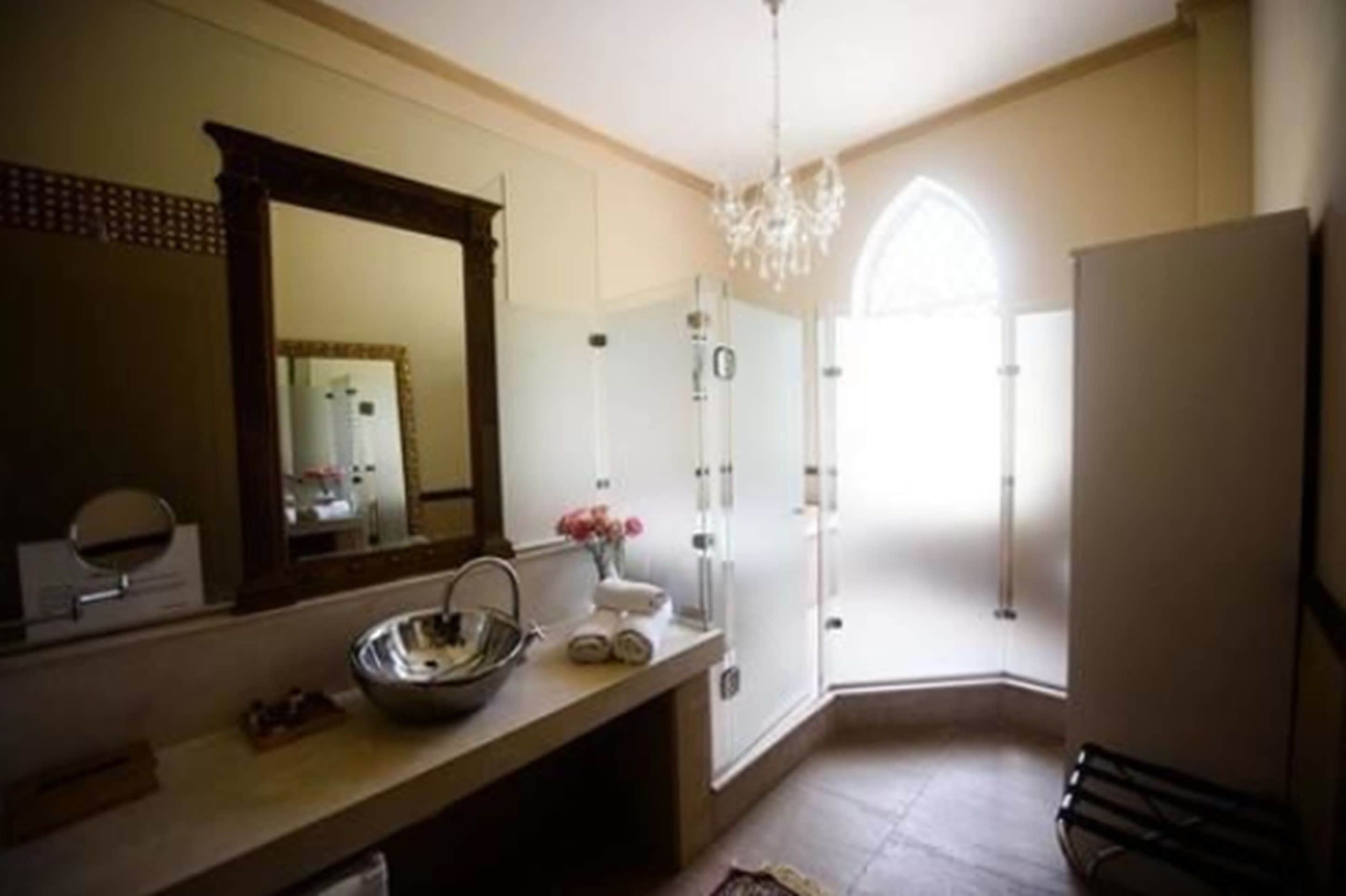 A bathroom with a large mirror, a sink with a bowl, a chandelier, and a shower area.