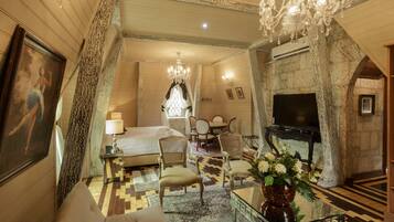 A spacious hotel room with a large bed, a sitting area with a sofa and chairs, a television, and a chandelier.