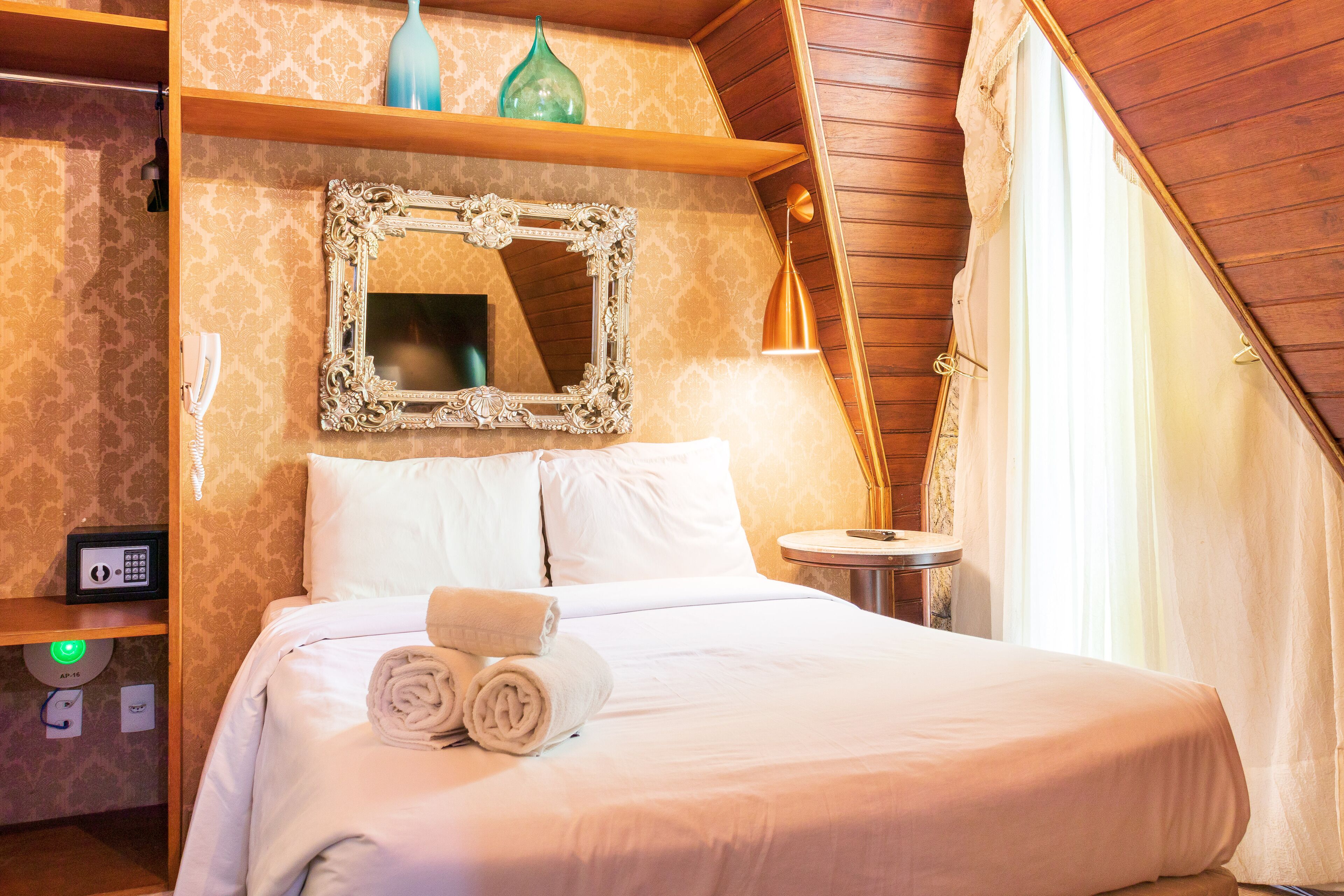 A hotel room with a large bed, a mirror, a bedside table, and a small round table.