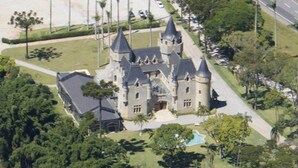 Un grand bâtiment imposant, qui ressemble à un château, avec de nombreuses tours et tourelles, entouré d’une végétation luxuriante et agrémenté d’une piscine.