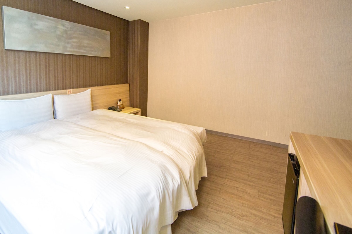 Quarto de hotel com uma cama grande, mesas de cabeceira, uma escrivaninha e uma televisão.