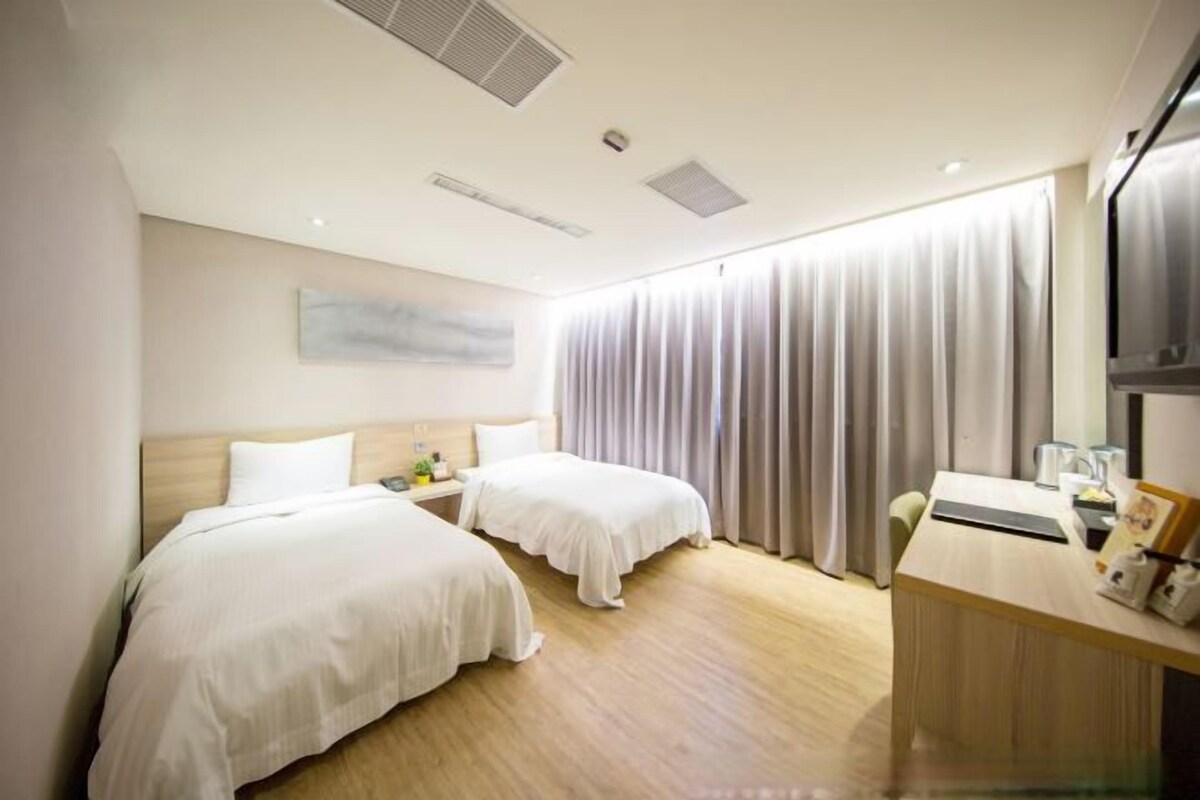 Una habitación de hotel con dos camas, un escritorio y un ventanal con cortinas.