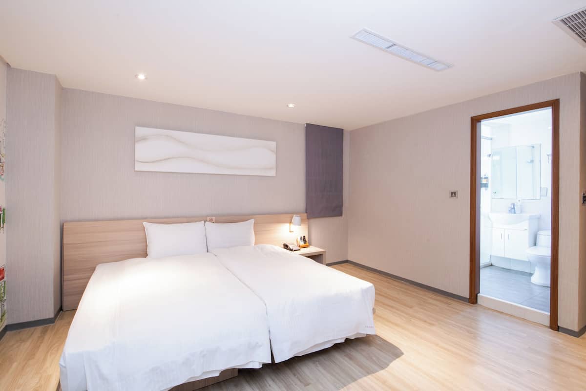 Quarto de hotel com uma cama grande, mesa de cabeceira e vista para o banheiro.