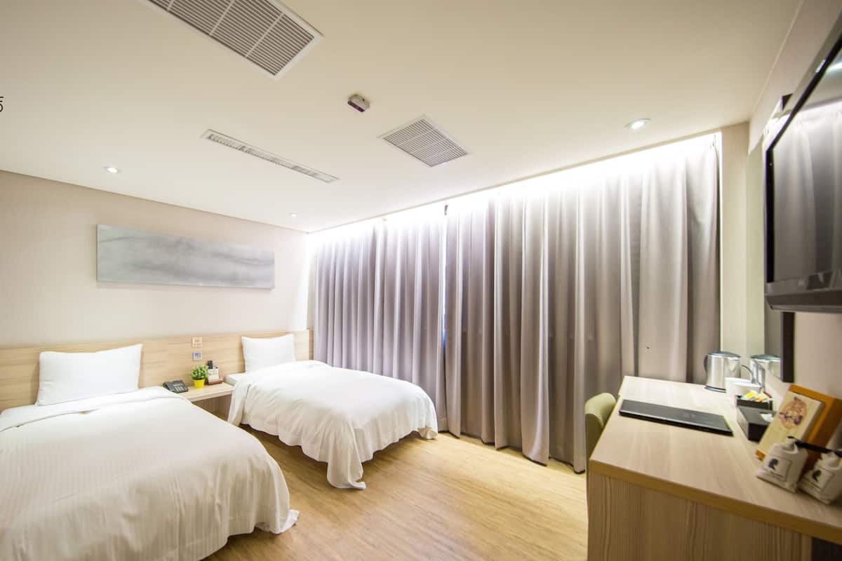 Quarto de hotel com duas camas, uma escrivaninha e uma televisão.