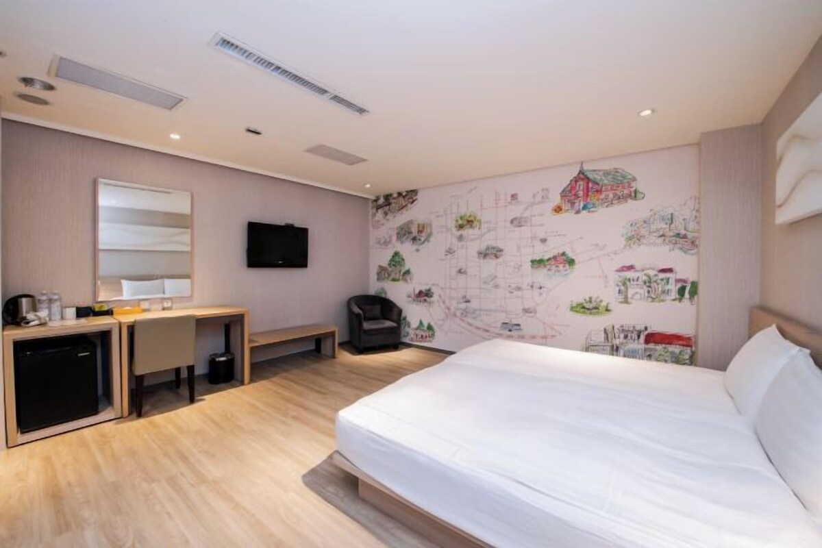 Una habitación de hotel con cama, escritorio, silla e ilustraciones en la pared.