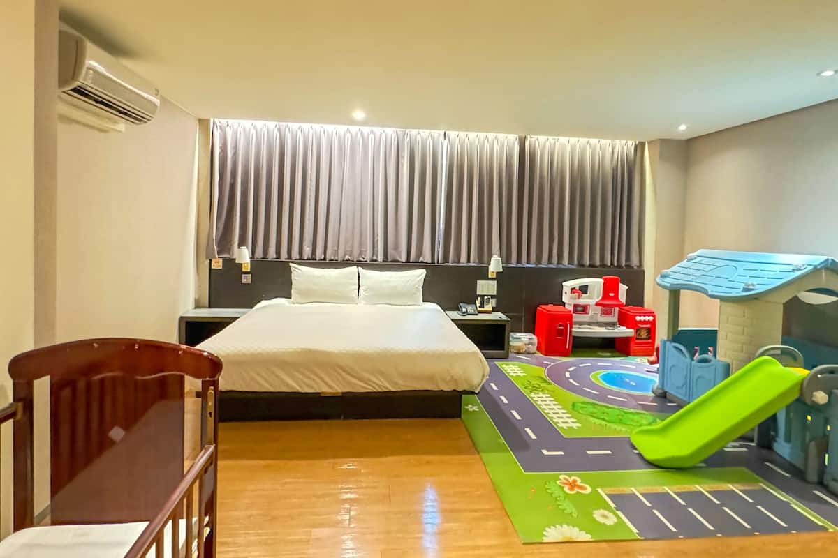 Quarto de hotel com cama, uma cadeira de madeira, área de recreação com escorrega e aparelho de ar condicionado.