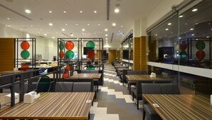 Moderni ravintola, jossa on useita ruokailutiloja, kuten erillisiä istuinalueita ja pöytiä, ja suurista ikkunoista avautuu näkymä kadulle.