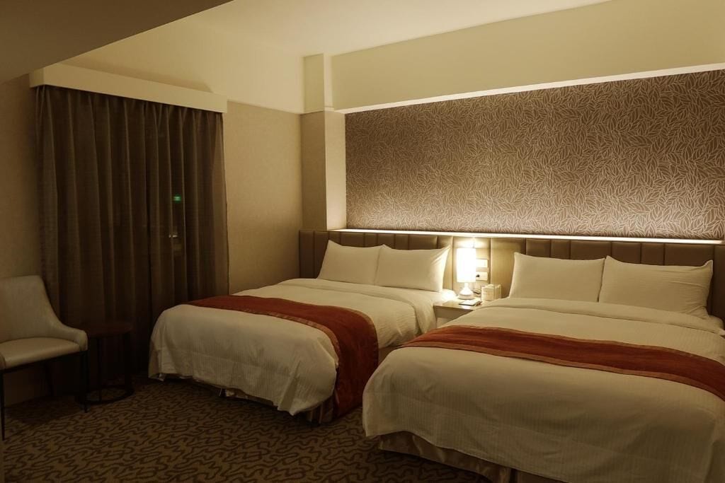 A hotel room with two beds, a chair, a patterned headboard, and a patterned carpet.