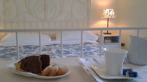 A neatly made bed with a floral bedspread, a bedside table with a lamp, and a plate with pastries and a slice of cake. - Luna Piena B&B (Lecce)