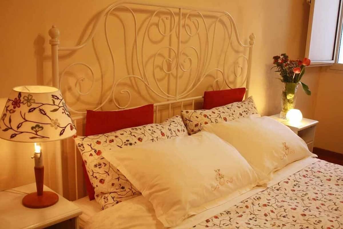 Uma cama bem arrumada com roupa de cama floral, uma cabeceira metálica decorativa e um abajur.