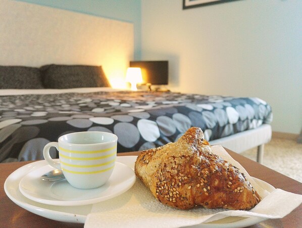 A bed with a patterned bedspread, a bedside lamp, and a cup and pastry on a table. - Luna Piena B&B (Lecce)
