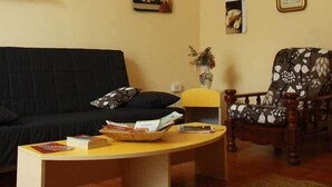 A living room with a black sofa, a wooden armchair, a yellow coffee table, and a hanging light fixture. - Luna Piena B&B (Lecce)