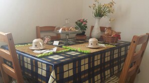 A dining table with a checkered tablecloth, two teapots, a vase with flowers, and a basket of bread. - Luna Piena B&B (Lecce)