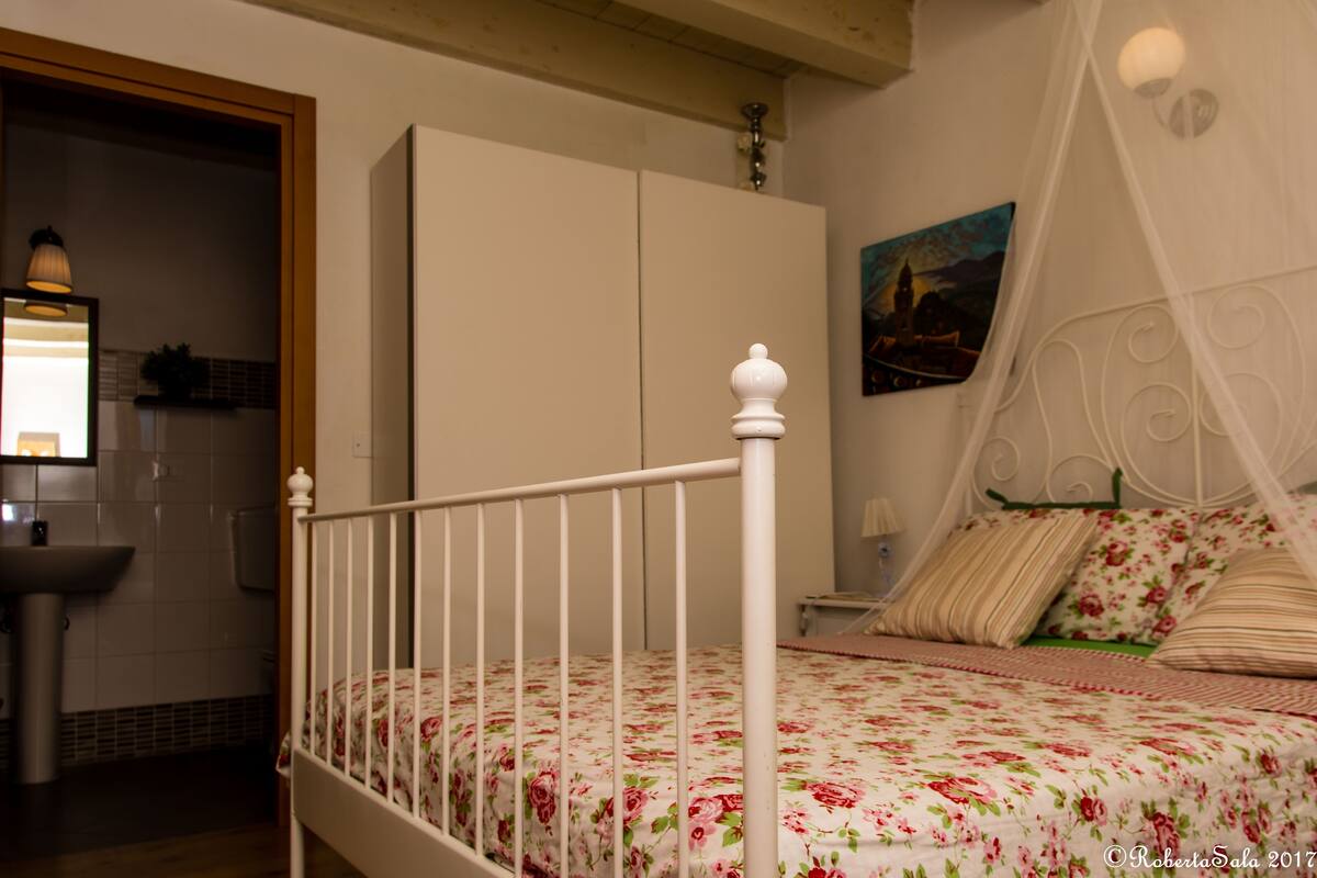 A bedroom with a bed, a nightstand, a bedside table, a mirror, a wardrobe, and a painting on the wall.