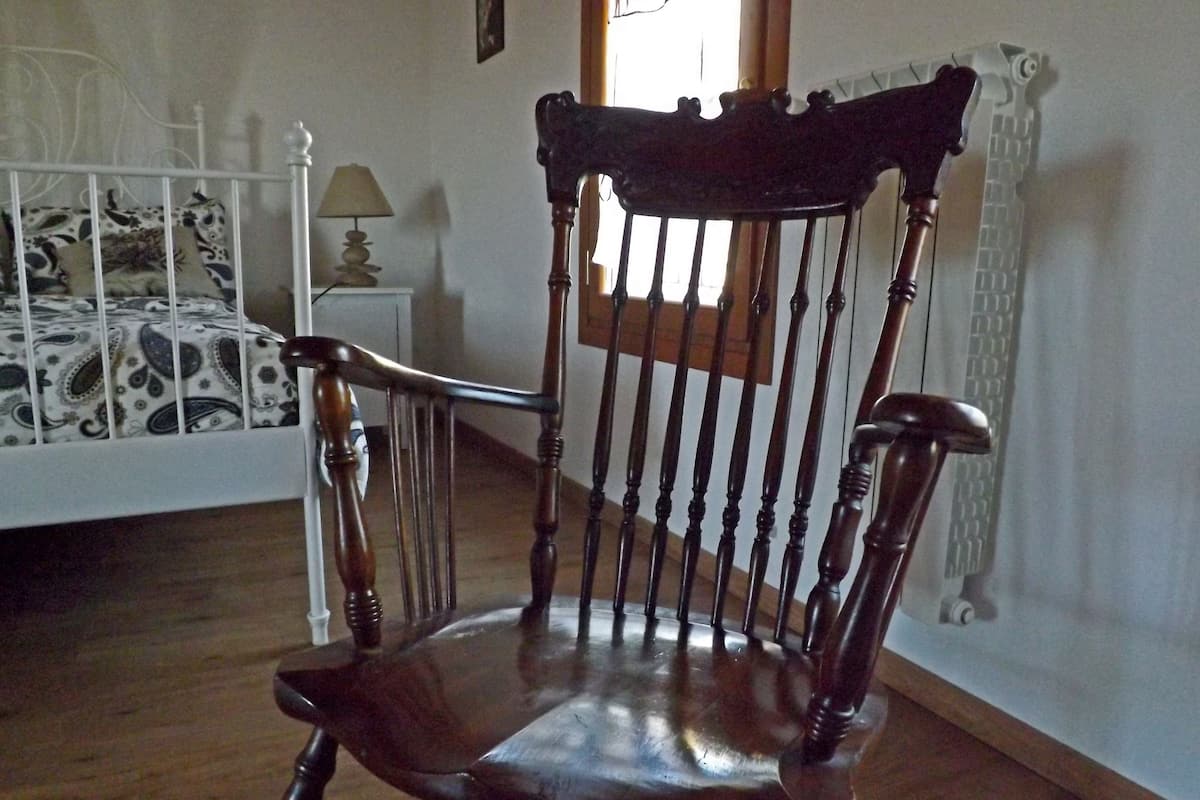 A wooden chair with a high backrest and armrests in a room with a bed and a nightstand.