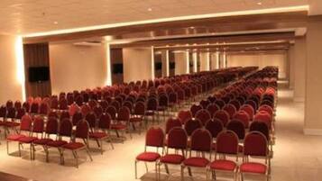 Une salle de conférence avec des rangées de chaises rouges et un plafond haut.