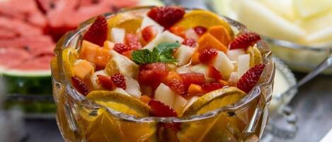 Un bufé con diversas frutas y un bol de ensalada de frutas.