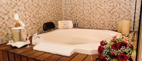 A hotel bathroom with a large bathtub, a sign indicating the hotel name, a bouquet of red roses, and a bottle of lotion.