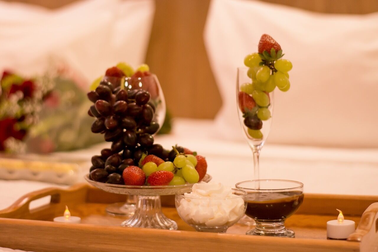 Een dienblad met diverse soorten fruit en een klein schaaltje slagroom, kaarsen en een glas donkere vloeistof, waarschijnlijk dessertwijn, op een tafel.