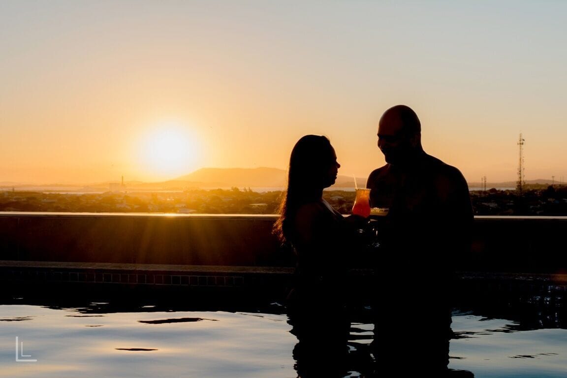 La silhouette d’un couple près d’une piscine au coucher du soleil, avec une vue sur la ville en arrière-plan.