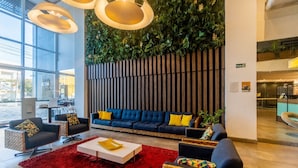 A modern hotel lobby with a blue sofa, red rug, and natural light from large windows. - Paradiso Corporate - Cabo Frio (Cabo Frio)