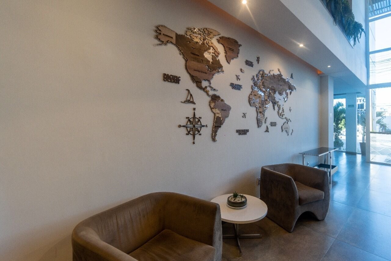 Un hall d’entrée orné d’une fresque représentant une carte du monde, deux fauteuils marron, une petite table ronde avec une plante et une cloison en verre.
