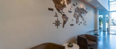 Un hall d’entrée orné d’une fresque représentant une carte du monde, deux fauteuils marron, une petite table ronde avec une plante et une cloison en verre.