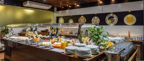 Een buffetopstelling met diverse gerechten en dranken, een groot eiland met een glazen blad, en decoratieve borden aan de muur.