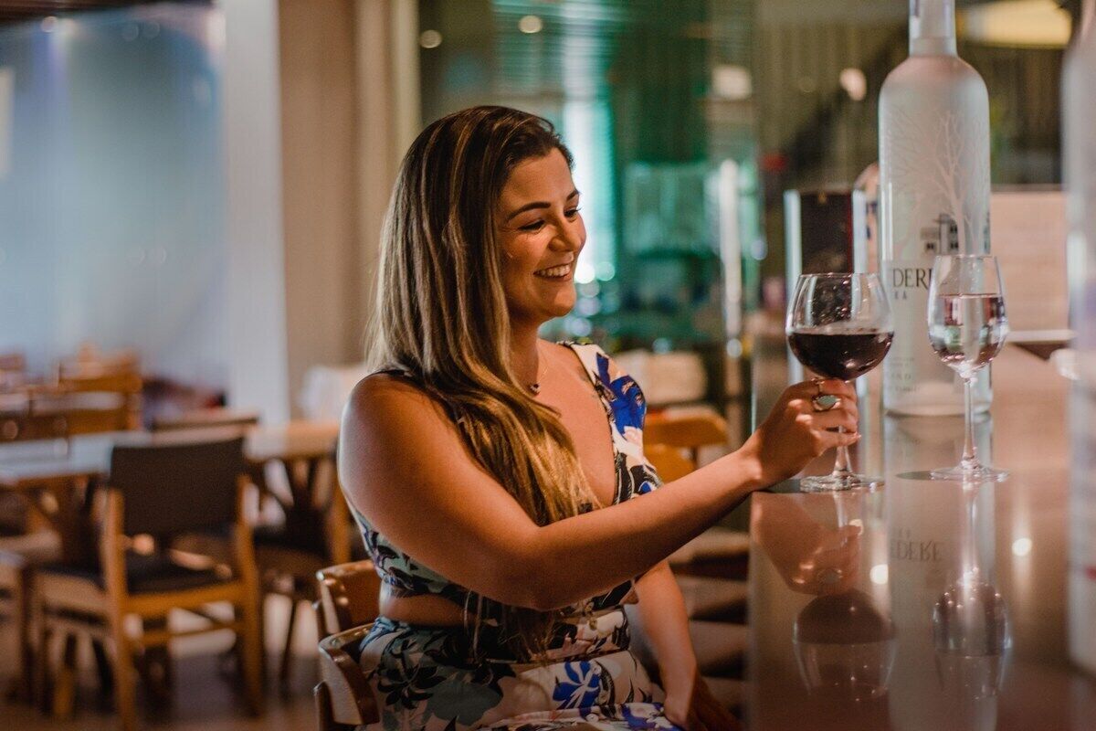A person seated at a table with a bottle and glasses, suggesting a dining or bar setting.