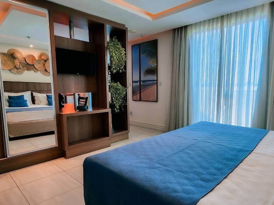 Ein Hotelzimmer mit Bett, einem großen Spiegel, einem Fernseher, einer Pflanze und Blick nach außen.