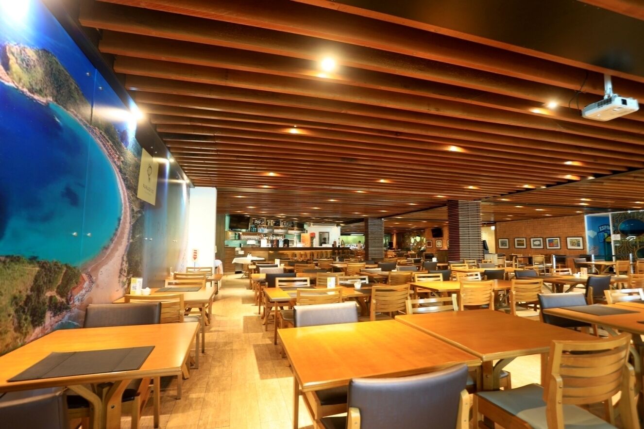 Un restaurante espacioso con mesas y sillas de madera, un gran mural en la pared y un diseño de techo moderno.