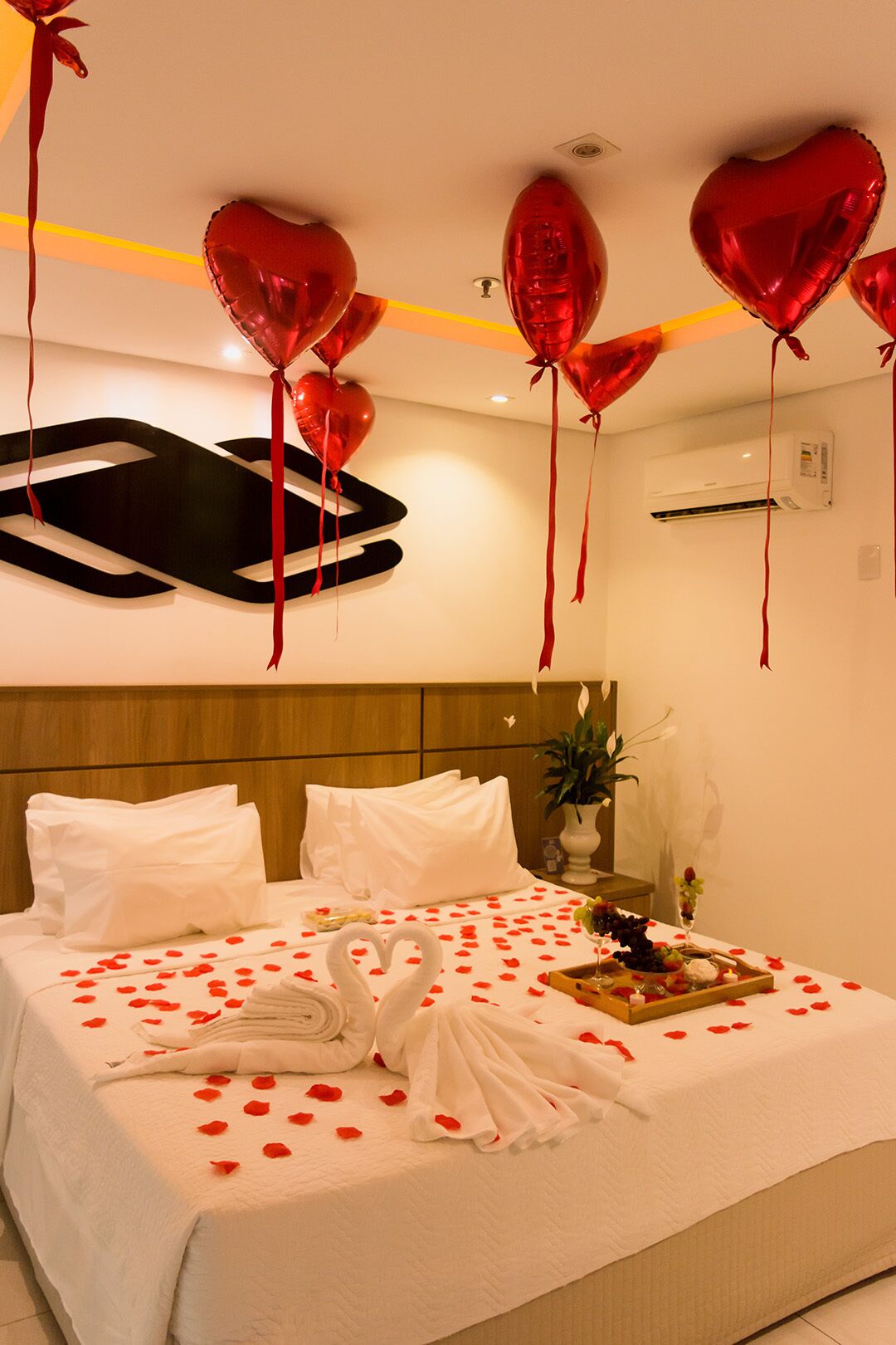 A hotel room with a bed adorned with rose petals, a tray of snacks, and a heart-shaped towel arrangement.