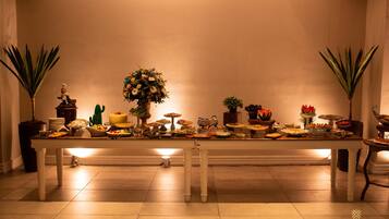 A long dining table with various dishes and centerpieces, flanked by potted plants.