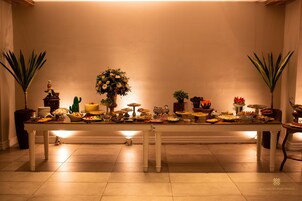 A long dining table with various dishes and centerpieces, flanked by potted plants.