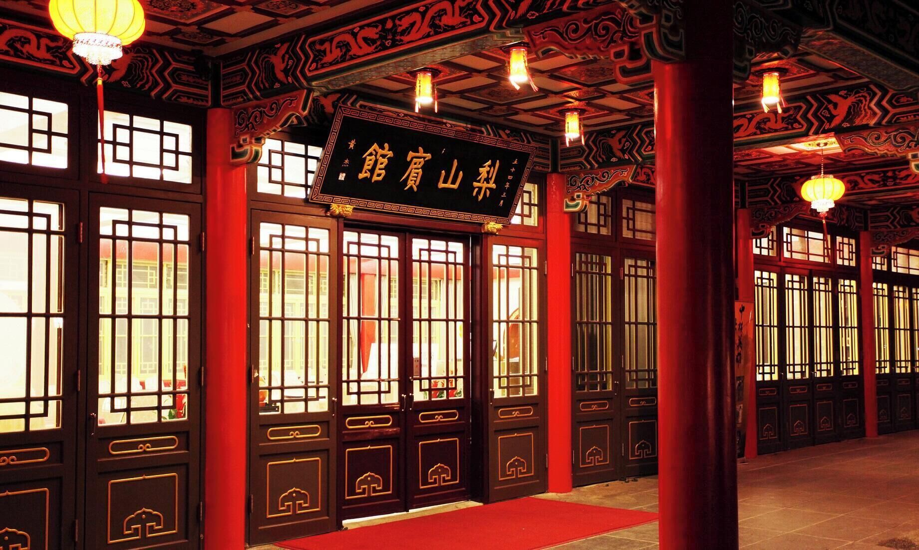 A traditional building with ornate red and black wooden doors, a sign with Chinese characters, and hanging lanterns.