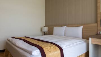 A hotel room with a neatly made bed, a bedside table with a lamp, and a wooden headboard.