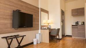 Et hotelværelse med et fladskærms-tv, et skrivebord med lampe, en stol, et lille skab og en skraldespand.