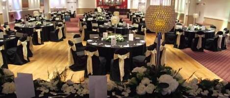 A banquet hall with round tables, black tablecloths, and white floral centerpieces.