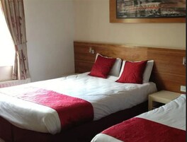 Cama doble con ropa de cama roja y blanca, cabecera de madera y mesita de noche pequeña.