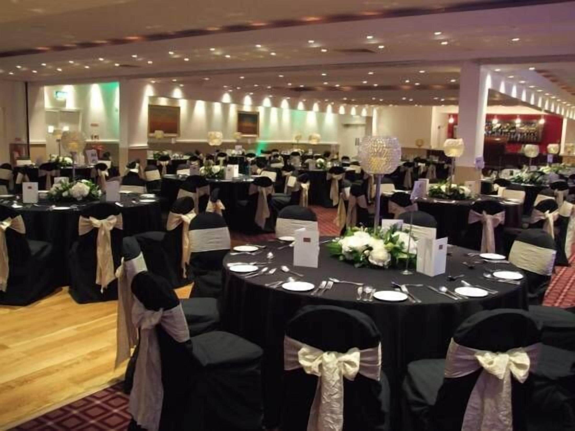A banquet hall with round tables set for dining, each with white tablecloths and centerpieces.