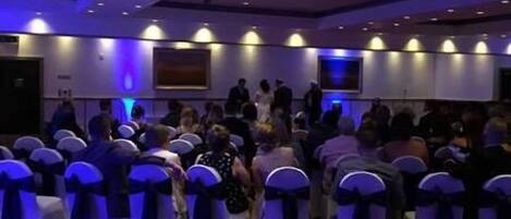 A conference room with rows of chairs, some with blue sashes, and a carpeted floor.