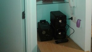 Una habitación pequeña con una pared verde azulada, un estante de vidrio con plantas en macetas, un teléfono blanco y un sistema de sonido negro.