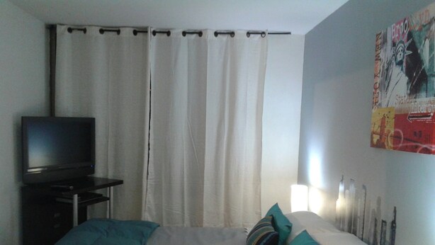 Un dormitorio con una cama, un televisor sobre un mueble y una cortina.