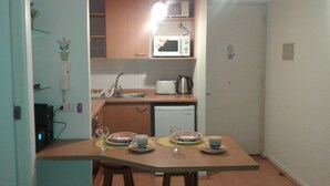 Cocina compacta equipada con microondas, tostadora y lavamanos. Cuenta con una mesa de comedor con sillas y un taburete pequeño.