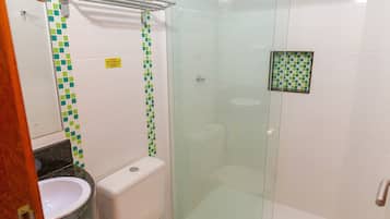 Un baño con ducha de vidrio, inodoro blanco y lavamanos con salpicadero de azulejos verdes y blancos.