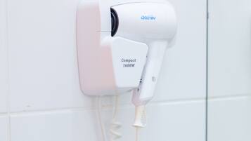 A hair dryer mounted on a wall with a coiled cord.