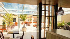 Un restaurante moderno con techo de cristal, mobiliario de madera y plantas en macetas.