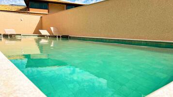 A swimming pool with clear water, surrounded by beige walls and a building with a tiled roof.